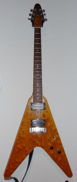 Fred V

Diese eigentlich originale 70er Jahre Gibson Flying V wurde extrem modifiziert. Das 70er Jahre Design lässt viel Platz zwischen Korpus-Oberfläche und Griffbrett Oberkante. Also hatte jemand die Idee, eine schöne Decke aufzukleben. Der Korpus ist nun von einem Binding eingefasst und die Tunomatic Brücke durch einen Wraparound-Steg ersetzt worden.
Ich habe sie von einem Gitarristen namens "Fred" bekommen, deswegen heisst das Teil bei mir immer die "Fred Vee". Er hat sie mir gegen ein Päckchen Saiten überlassen. Allerdings war sie da komplett nackt und die Kopfplatte abgebrochen. Aber damit hatte ich ja schon Erfahrung und hab mit einer dünnen Lage Glasfaser abgeholfen, Die Stelle ist nun etwas rau, aber es wurd keine deckende Neulackierung nötig, was ja auch sehr schade gewesen wäre.
Die Pickups sind welche, die ich zu der Zeit aus anderen Gitarren ausgebaut hatte, weil sie mir dort nicht gefielen. Hier machen sie aber eine gute Figur: ein SH-8 "Invader" und ein OBL.